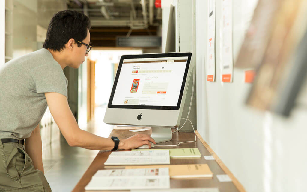 Postgraduate student Darryl Lim looking at student displays of work including digital and printed projects