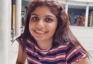 A young woman smiling. She has long dark hair and is wearing a striped top.